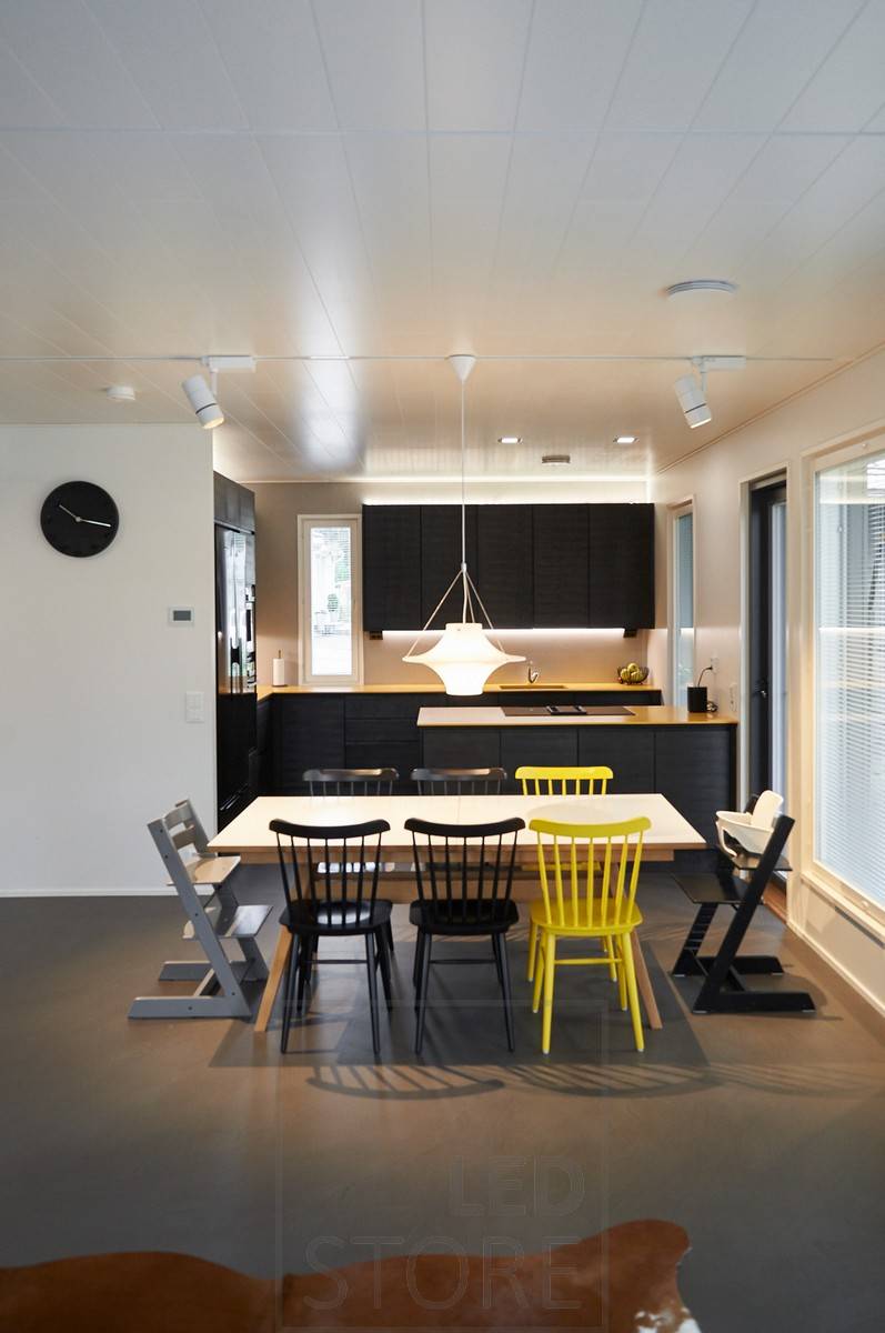 Luminaire sur rail FOKUS dans un rail triphasé pour un éclairage général efficace dans la salle à manger, avec un luminaire Lokki sur la table à manger. Bandes de leds éclairant la cuisine d'une lumière indirecte. Ledstore.fi